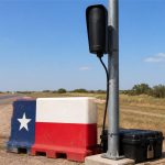 Cámara vial Flock detenida junto a una barrera en una carretera de Texas