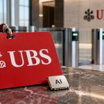 Credencial roja de UBS junto a un chip de IA y una barrera de acceso bancaria desenfocada
