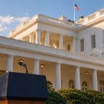 Vista oblicua de la Casa Blanca con un atril institucional en primer plano