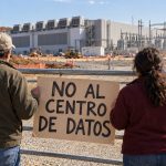Vecinos frente al acceso de una obra de centros de datos con un cartel de rechazo